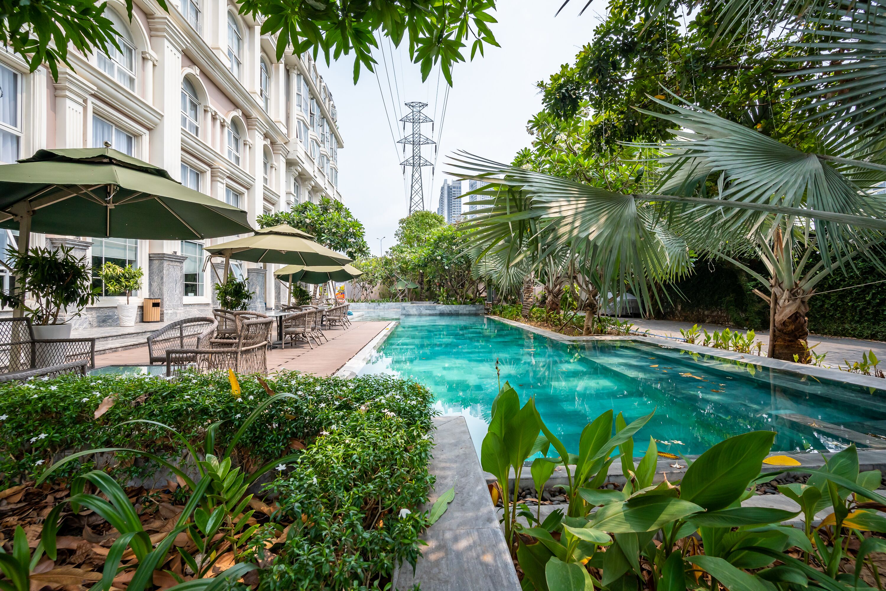 A pool area with lounge chairs and umbrellas, surrounded by lush greenery and a building with classical architecture.