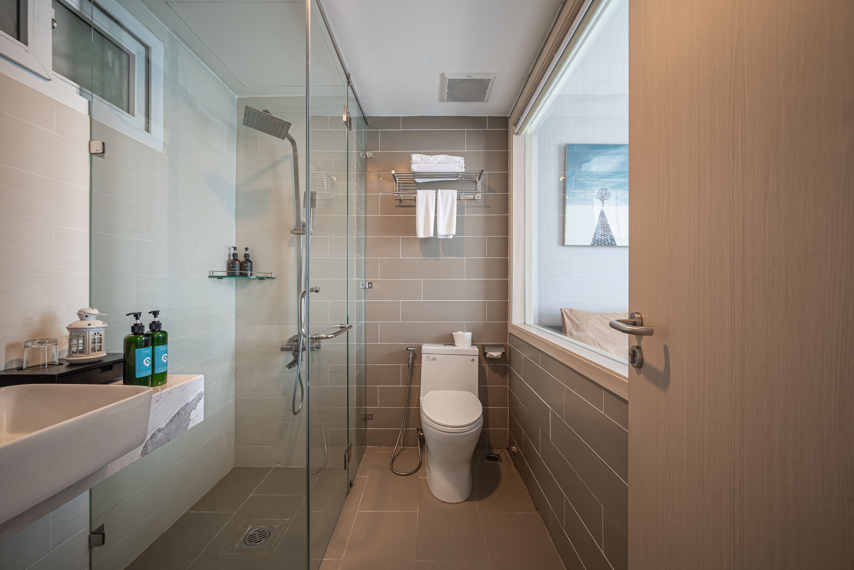 Un baño moderno con cabina de ducha de vidrio, inodoro blanco y un amplio ventanal que proporciona luz natural.