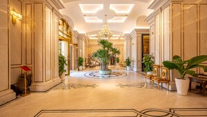 Eine prächtige Lobby mit Marmorböden, einem zentralen Kronleuchter und symmetrisch gestalteten Wandverkleidungen.