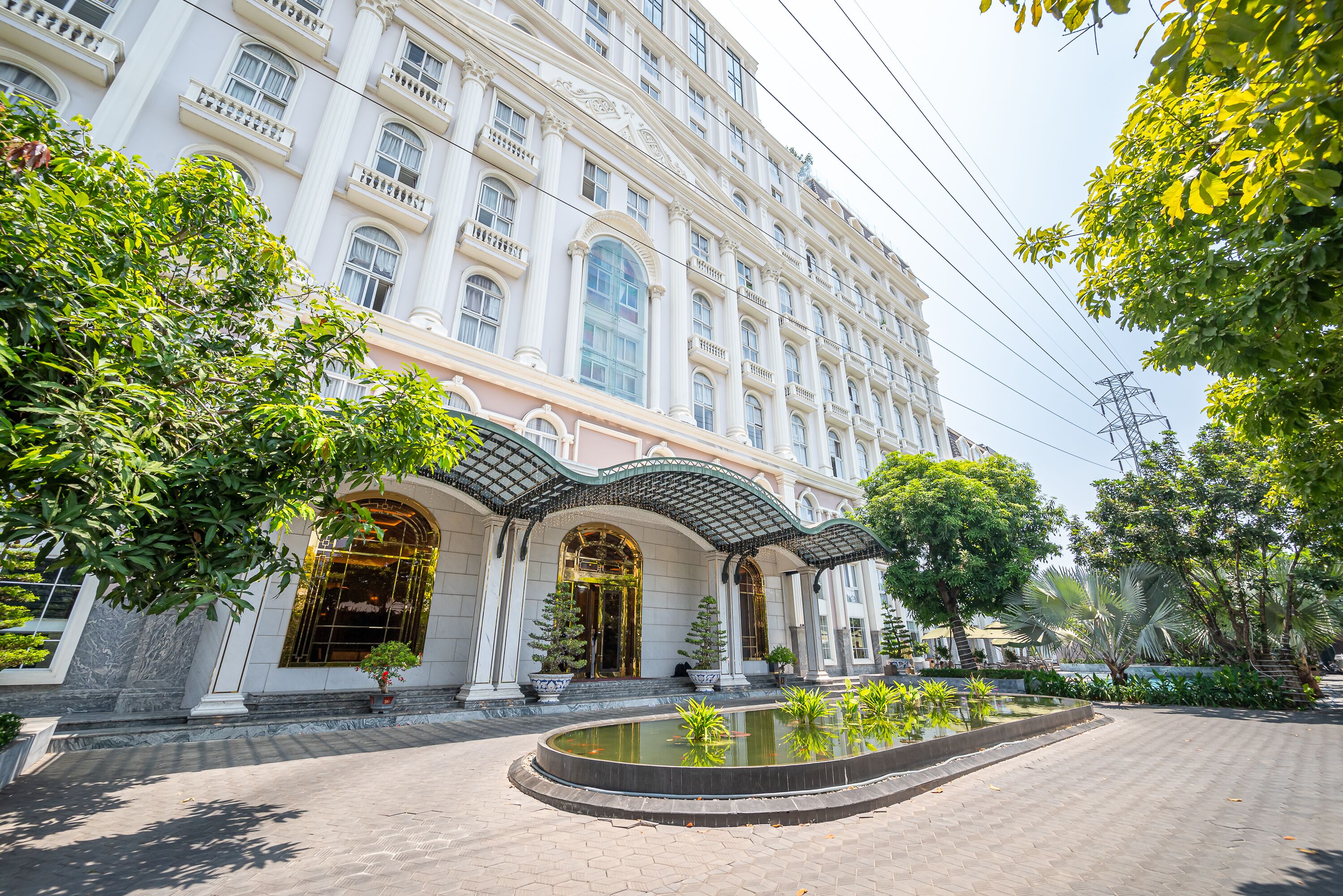 A large, classical building with a grand entrance, a fountain, and lush greenery.