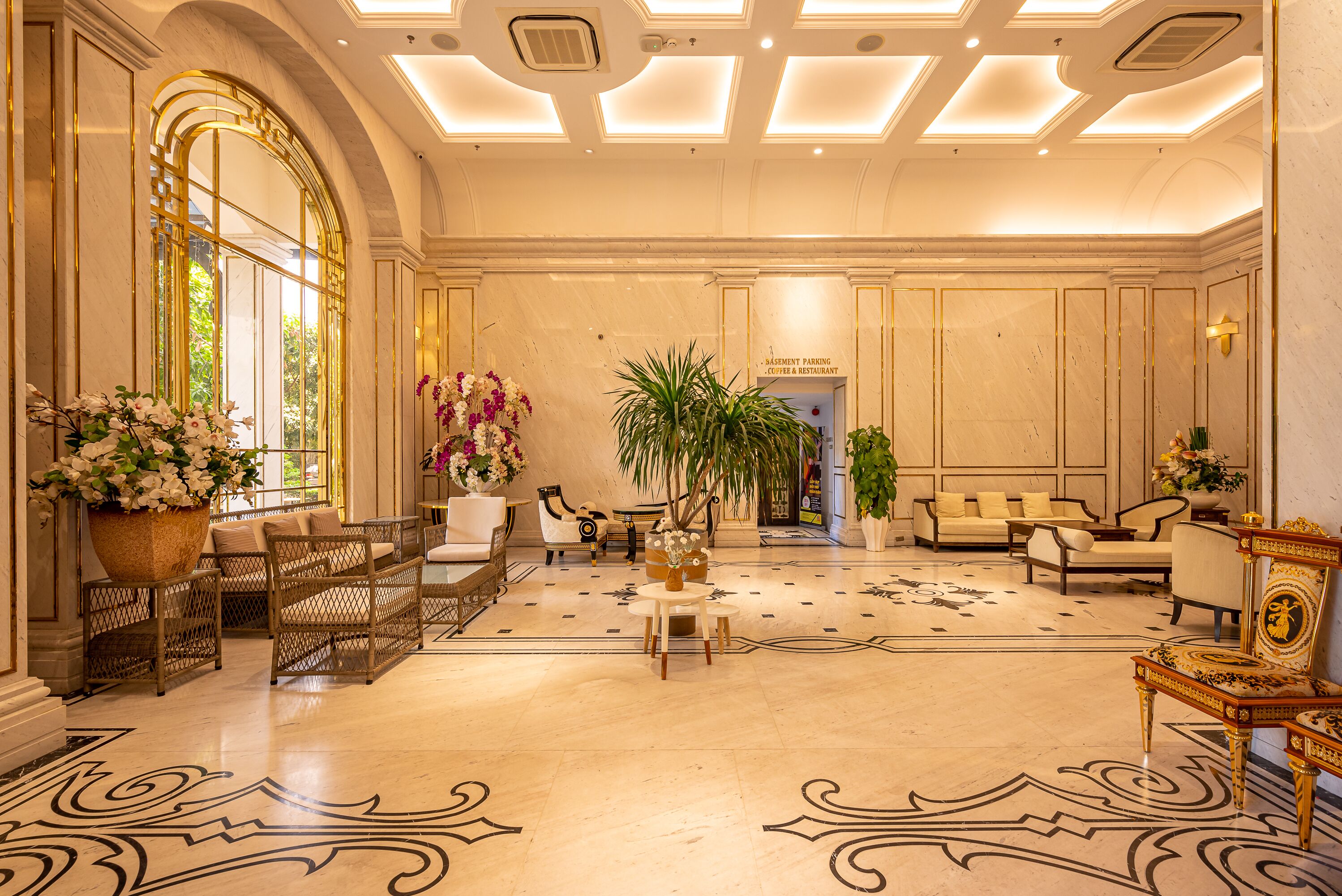 A spacious lobby with a large seating area, a reception desk, and a view of the entrance to the basement parking and restaurant.