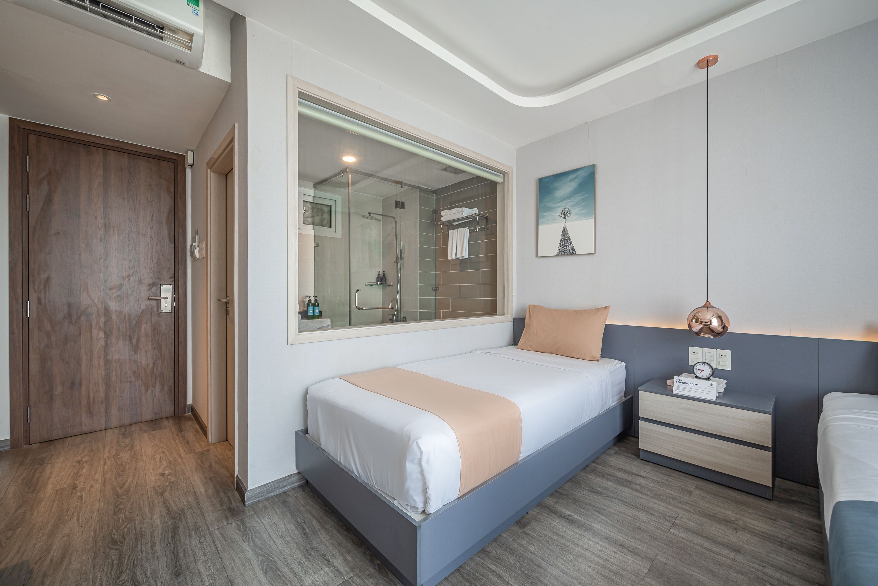 A modern bedroom with a large bed, a bedside table with a clock, and a window with a view of the bathroom.