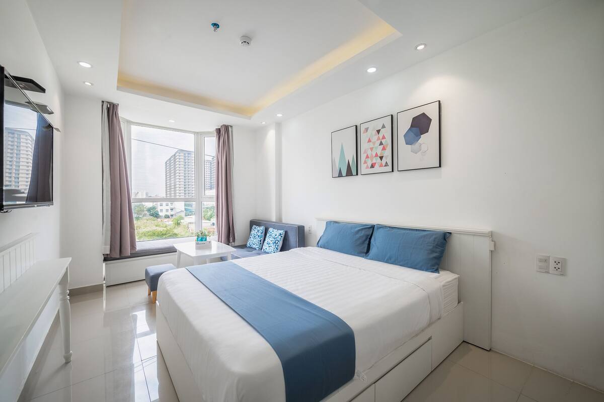 A modern hotel room with a large bed, a desk, and a window with curtains.