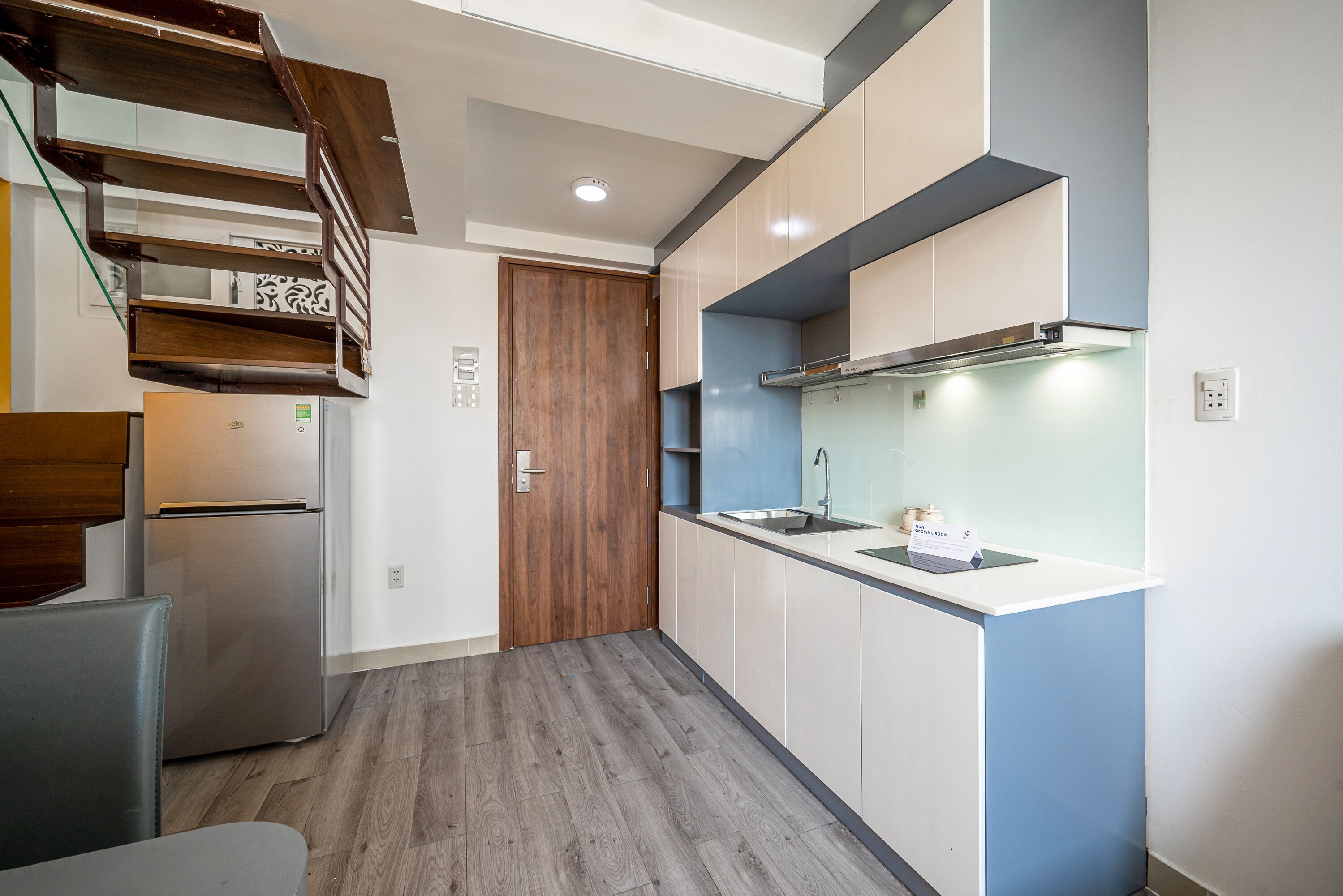 A compact kitchen with a built-in stove, a sink, and a wooden staircase.