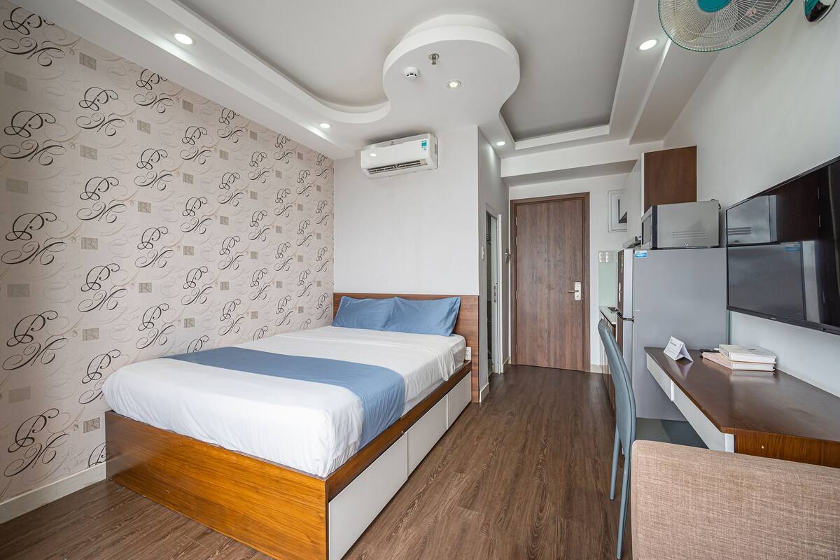 A modern bedroom with a wooden bed, a desk with a computer, and a TV.