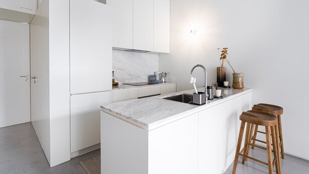 Une cuisine moderne avec des meubles blancs, un plan de travail en marbre, un évier en acier inoxydable et des tabourets en bois.