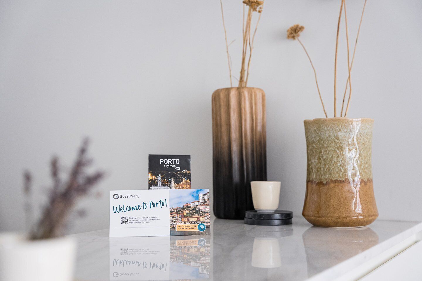 A welcome card for Porto, a city map, a ceramic mug, and two vases with dried plants.