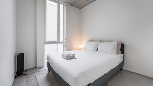 Une chambre à coucher moderne avec un grand lit, un radiateur, une fenêtre et une lampe de chevet.