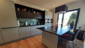 A modern kitchen with grey cabinets, a black countertop, and a large island with bar stools. - Villa in Winterberg near the ski area (Winterberg)