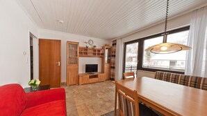 A modern living room with a wooden dining table, red sofa, and a television. - Allgäu Family Retreat (Nesselwang-Reichenbach)