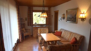 A cozy room with a wooden dining table, a sofa, and two chairs. There is a window with curtains and a painting on the wall. - Comfort with Garden Views (Füssen)