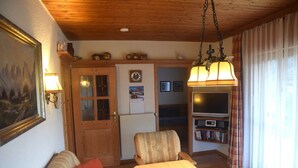 A cozy living room with a wooden ceiling, a sofa, a table, and a television. - Comfort with Garden Views (Füssen)