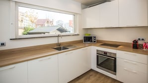 Una cocina moderna con armarios blancos, encimera de madera, horno empotrado, microondas y ventana con vistas a una zona residencial.