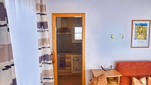 Una sala de estar con un sofá, una mesita, un cuadro enmarcado y una cocina visible a través de un umbral abierto.
