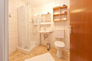 Une salle de bain équipée d’une douche, d’un lavabo, de toilettes et d’une étagère en bois.