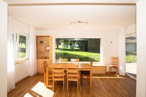 Une pièce comprenant une table à manger en bois, des chaises, une bibliothèque intégrée et une grande fenêtre donnant sur un espace verdoyant.