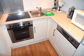Cocina compacta con estufa, pileta y lavavajillas, con alacenas blancas y piso de madera.