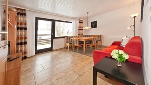 Ein modernes Wohnzimmer mit Esstisch, rotem Sofa und einem schwarzen Couchtisch mit Vase.