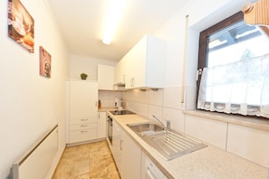 Una cucina compatta con mobili bianchi, un lavello in acciaio inossidabile e una finestra con tende in pizzo.
