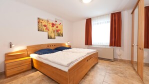 Quarto com cama de madeira, mesa de cabeceira, cômoda e radiador.