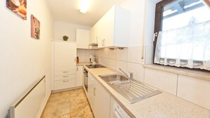 Uma cozinha compacta com armários brancos, uma pia de aço inoxidável e uma janela com cortinas de renda.