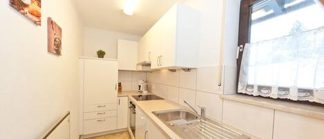 A compact kitchen with white cabinets, a stainless steel sink, and a window with lace curtains.