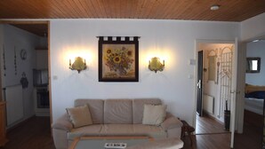 A living room with a beige sofa, a coffee table, and a painting of sunflowers on the wall. - Garden Apartment in Füssen (Füssen)