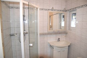 Bathroom features a glass-enclosed shower, handheld showerhead, and wall-mounted faucet.