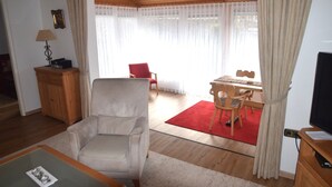 A living room with a sofa, a wooden cabinet, a TV stand, and a dining area with a table and chairs. - Garden Apartment in Füssen (Füssen)