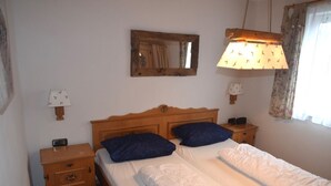 Un lit double avec une tête de lit en bois, deux tables de chevet avec des lampes, une commode, un miroir au mur et une fenêtre avec des rideaux.
