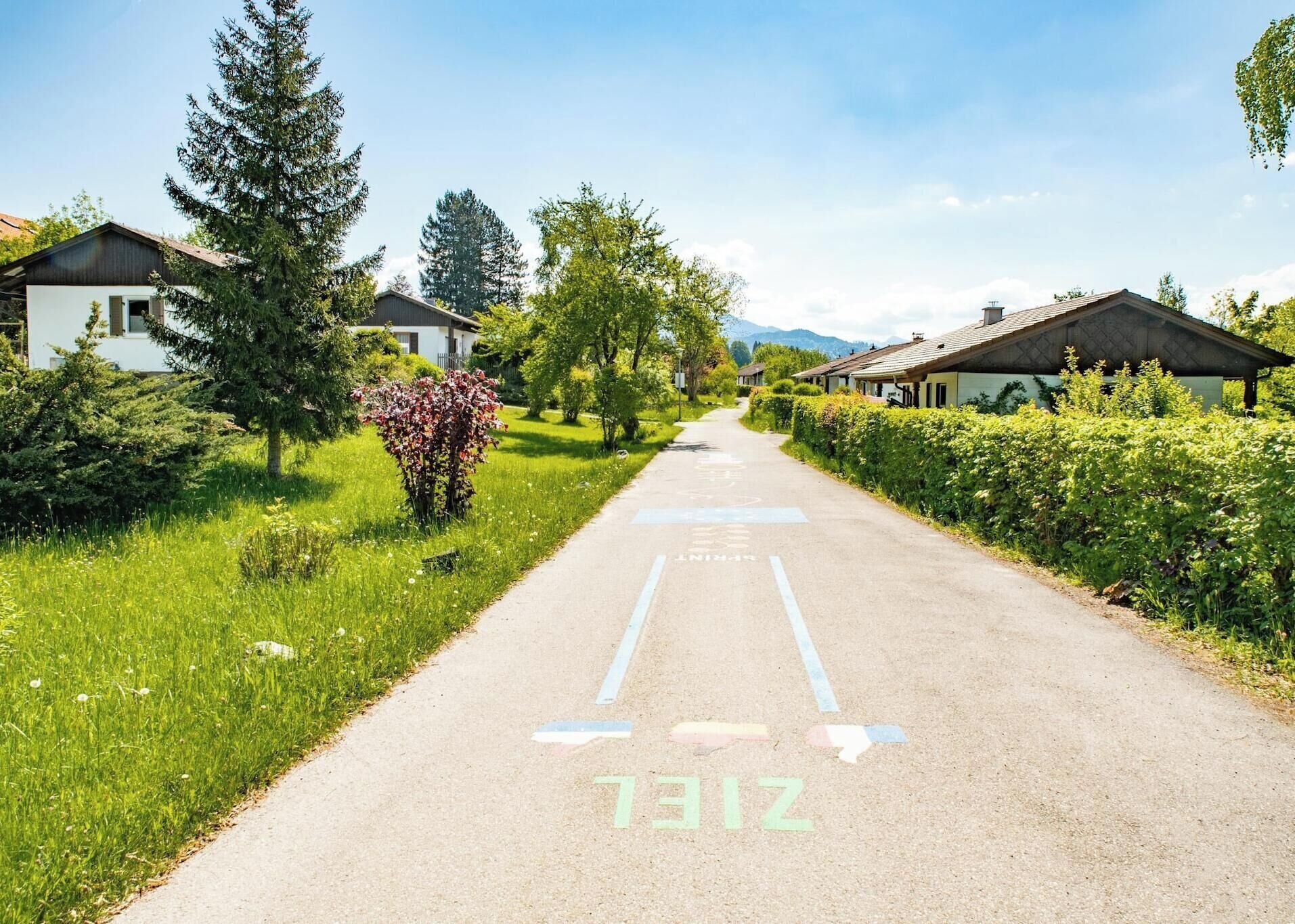 A residential street with houses on both sides, a clear sky, and a road with directional arrows.