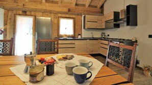 A wooden interior with a kitchen area, including a refrigerator, cabinets, and a dining table with cups and a coffee pot.