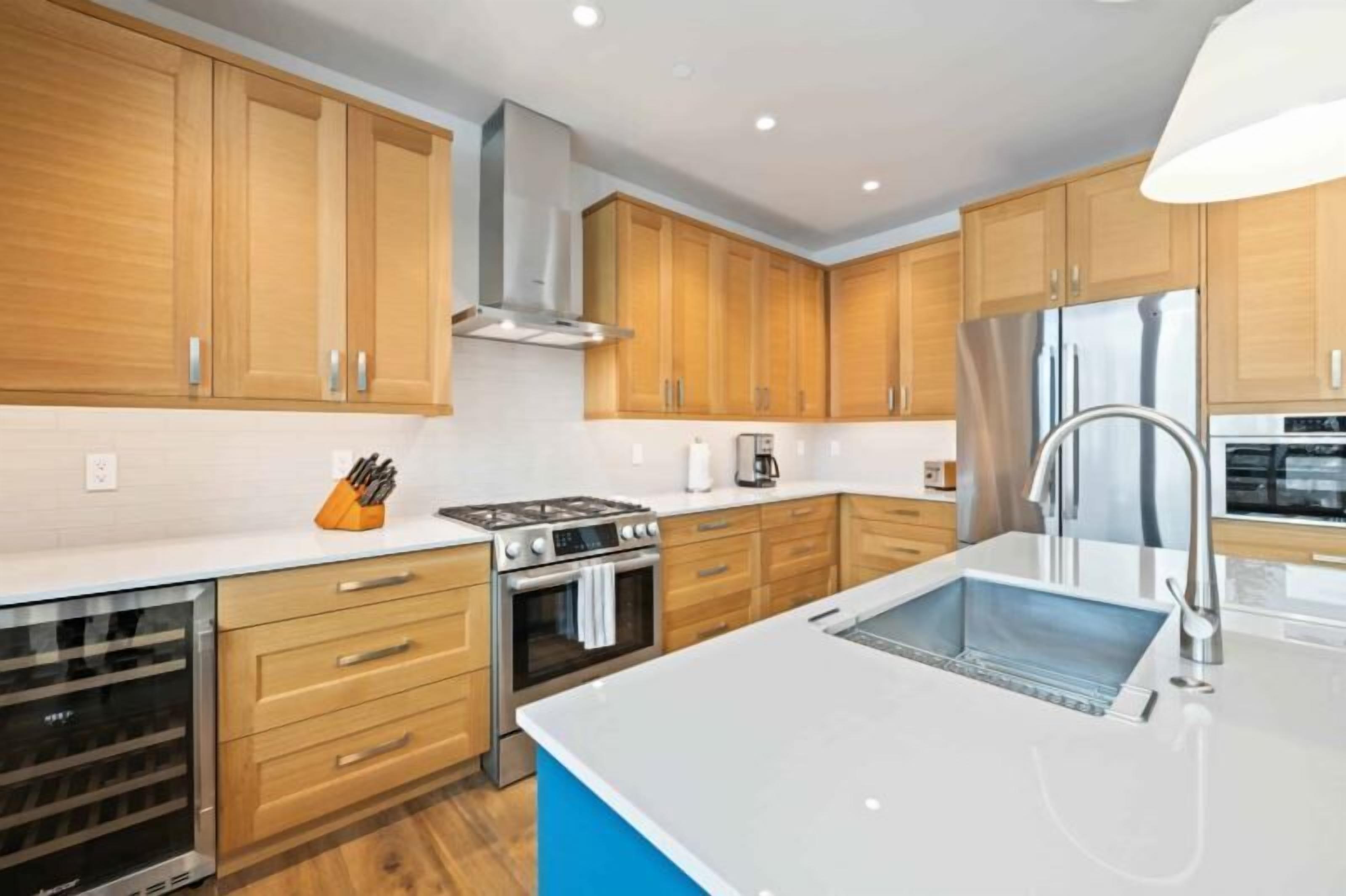A modern kitchen with wooden cabinets, stainless steel appliances, and a blue accent wall.