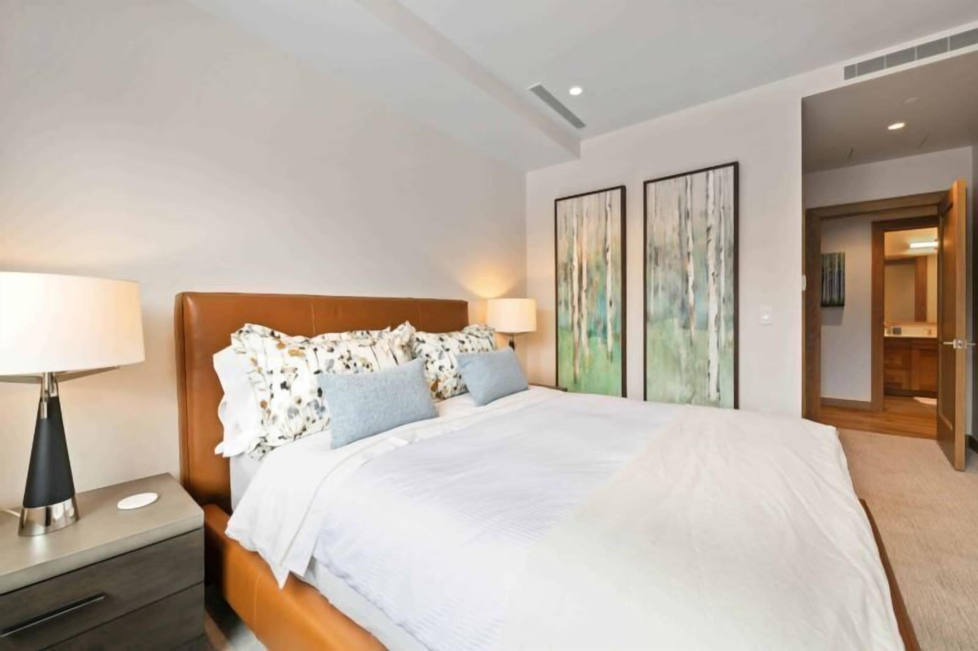 Een moderne hotelkamer met een groot bed, een nachtkastje met een lamp, en twee abstracte schilderijen aan de muur.