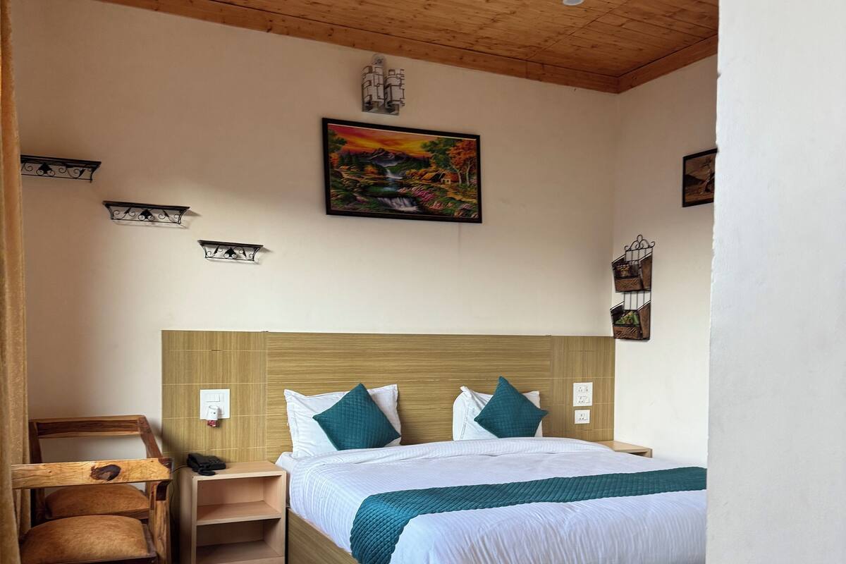 Quarto com cabeceira de madeira, cama com roupa de cama branca e almofadas verde-água, mesa de cabeceira, uma cadeira, um quadro na parede e um ventilador de teto.