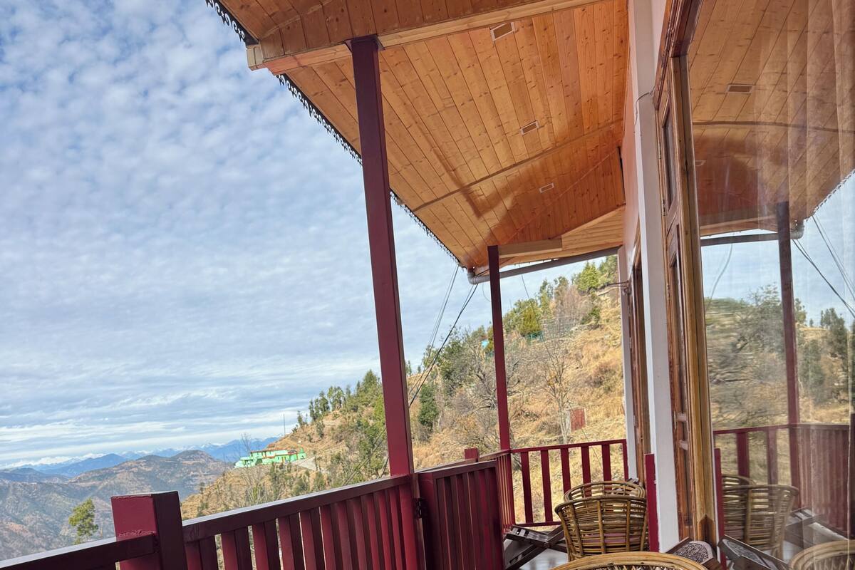 Varanda com mobiliário de vime e mesa de vidro, com vista para uma paisagem montanhosa.