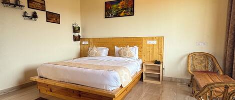 Un dormitorio con estructura de madera, una cama, un ventilador de techo, un cuadro y una zona de comedor con mobiliario de mimbre.