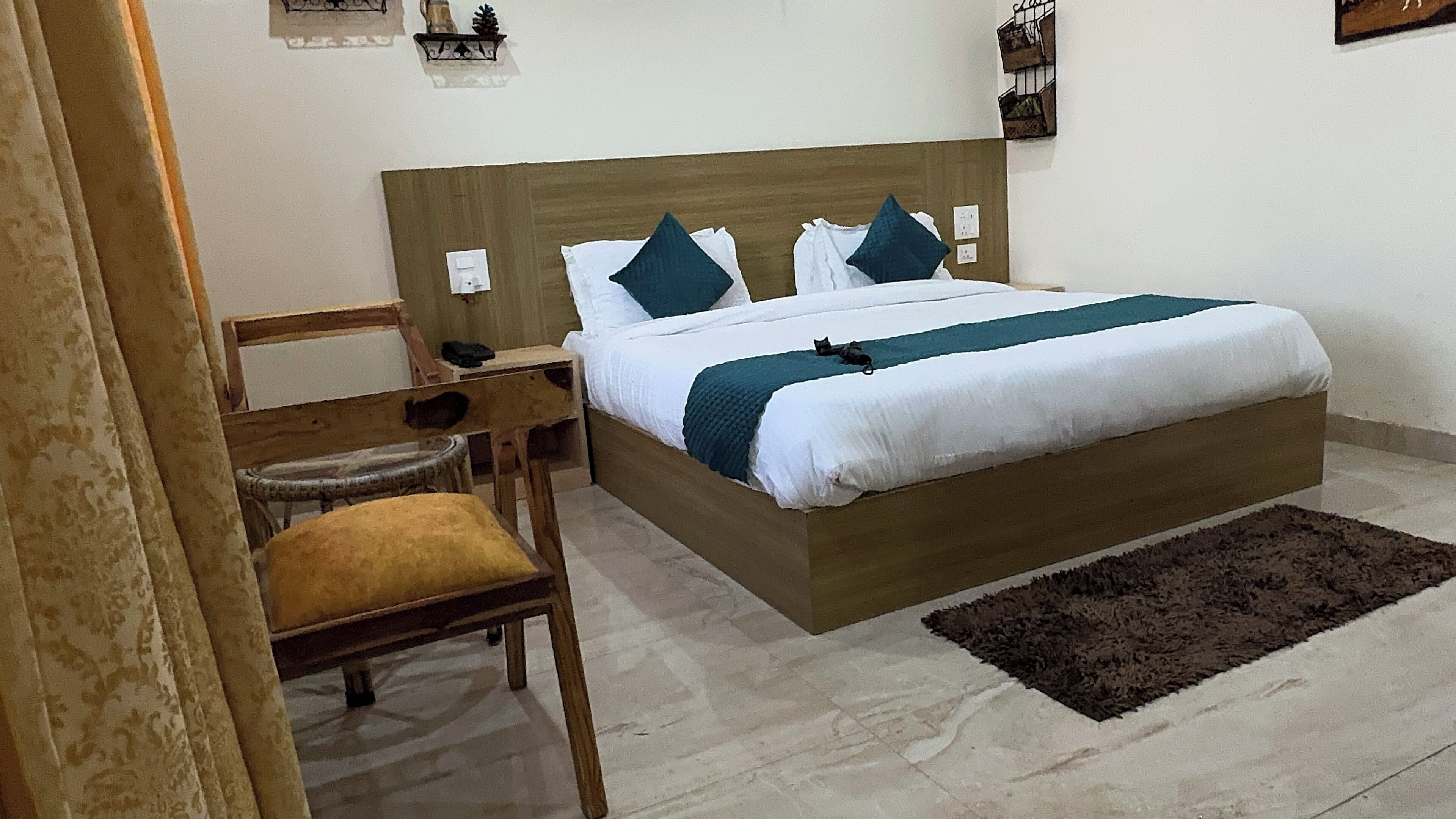 A neatly arranged bedroom with a wooden bed, white bedding, a dark rug, and a chair with a cushion.