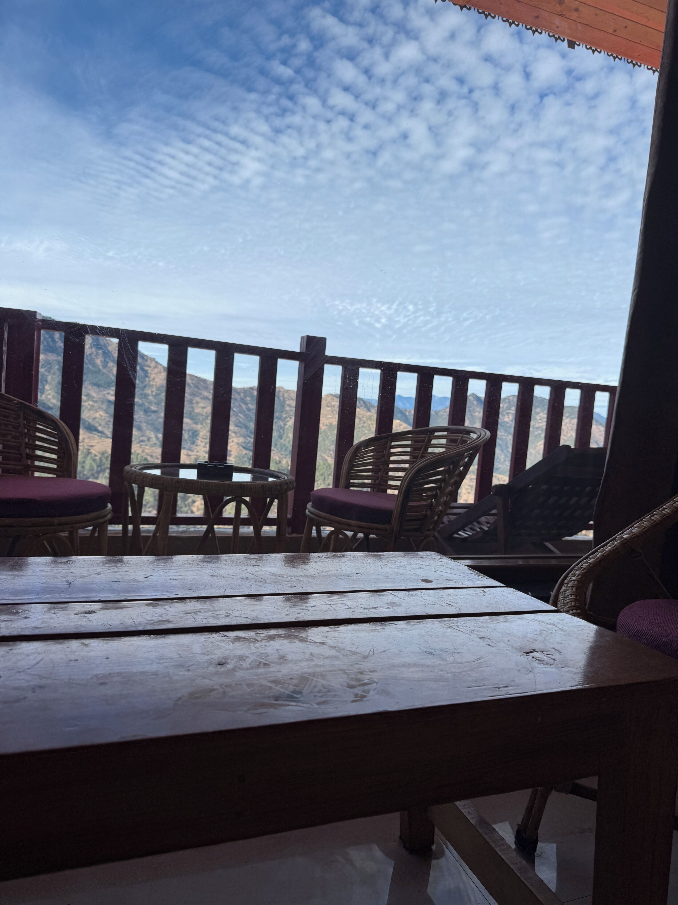 A wooden table and wicker chairs on a balcony with a mountain view.