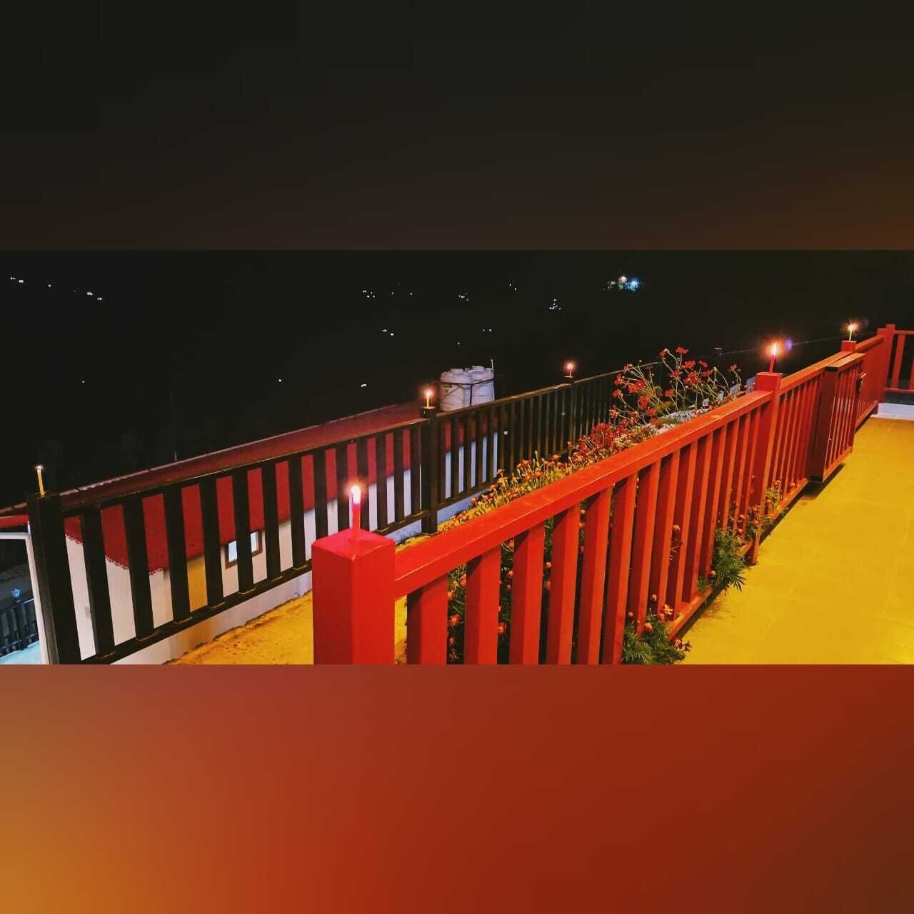 Varanda com guarda-corpo vermelho e chão amarelo, com vista para um céu noturno escuro.