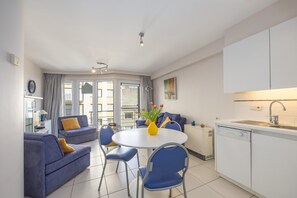 A modern living room with a round dining table, blue sofas, and a kitchen area with white cabinets and a sink. - Well-maintained apartment with sea view (Middelkerke)