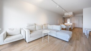 A modern living room with a sectional sofa, a small round table, and a kitchen area in the background. - Luxurious apartment with stunning sea view (Middelkerke)