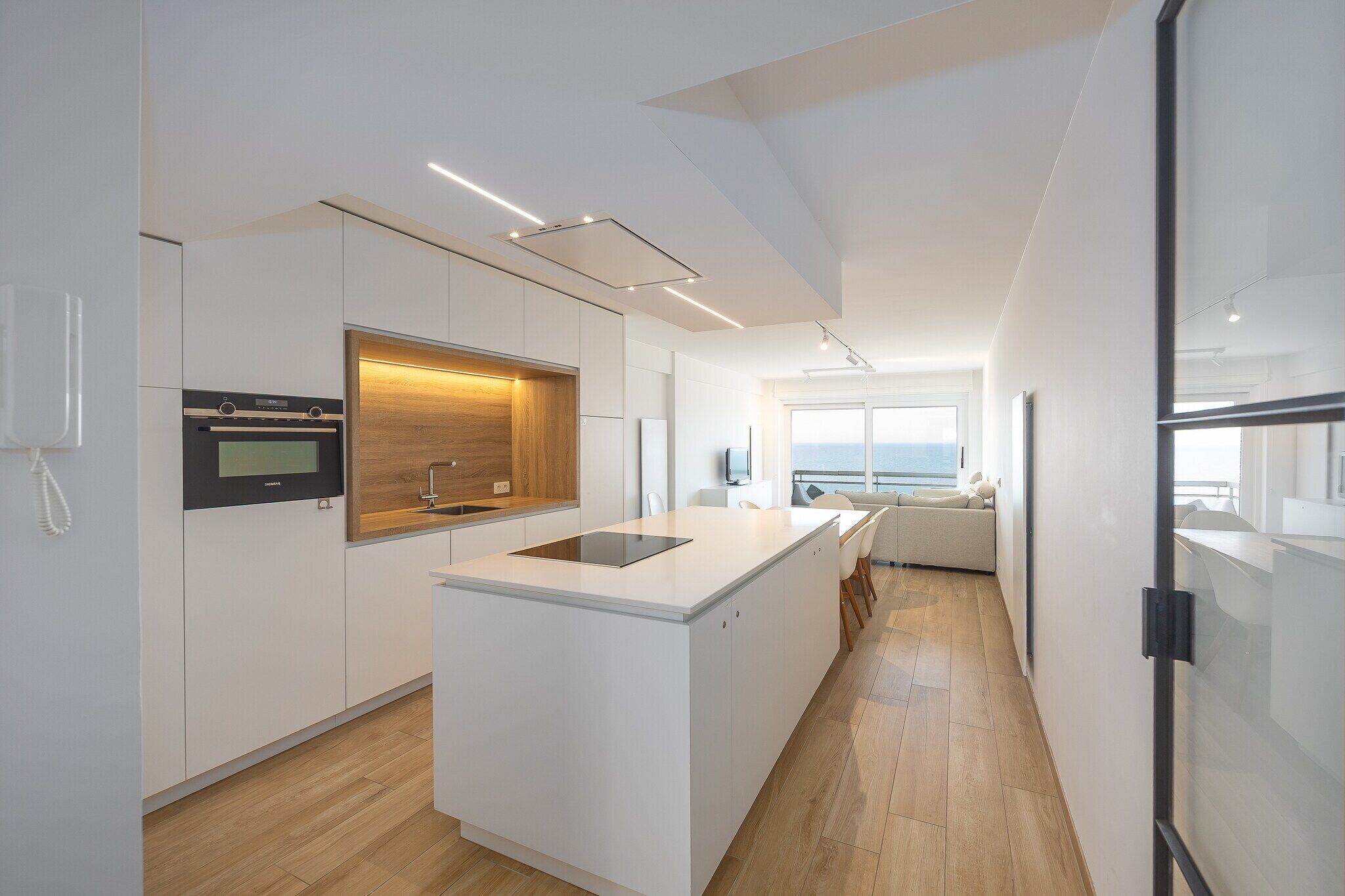 A modern kitchen with a central island, built-in oven, and a large window offering a view.