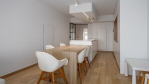 A modern kitchen with white cabinetry, a wooden dining table, and white chairs. - Luxurious apartment with stunning sea view (Middelkerke)