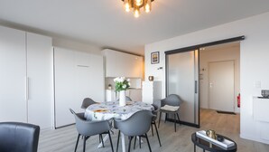A modern dining area with a table set for four, surrounded by grey chairs, a vase with flowers, and a small side table with decorative items. - Cosy studio with sleeping area and sea view (Middelkerke)