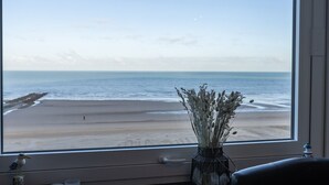 A view of the beach through a window, with a vase of dried flowers on the windowsill. - Cosy studio with sleeping area and sea view (Middelkerke)