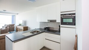 A modern kitchen with white cabinets, a built-in oven, and a coffee maker. - Beautiful apartment with phenomenal sea view (Westende)