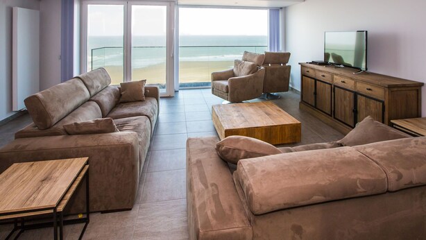 A modern living room with a large sofa set, a wooden coffee table, and a television on a wooden cabinet. - Beautiful apartment with phenomenal sea view (Westende)