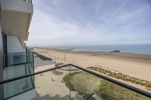 A beach view from a balcony with a clear sky, a sandy beach, and a few people walking. - Beautiful apartment with phenomenal sea view (Westende)