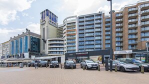 Ein modernes Hotel mit mehreren Etagen, einem markanten Eingang und mehreren parkenden Autos davor.